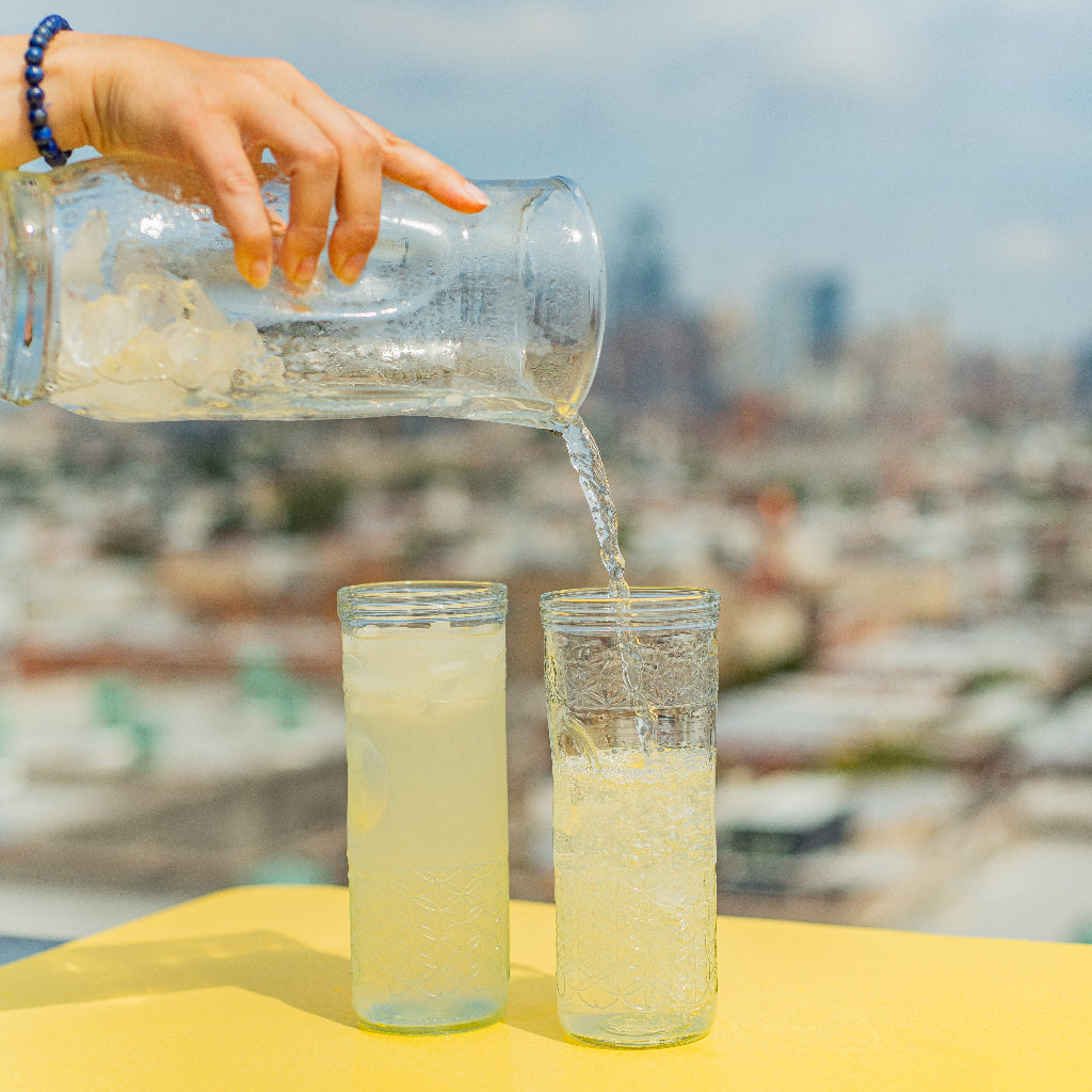 Person pouring lemonade into two glasses with a cityscape in the background