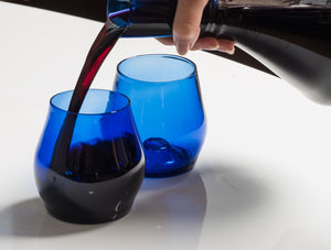 two dark blue short glasses, one of them being poured into