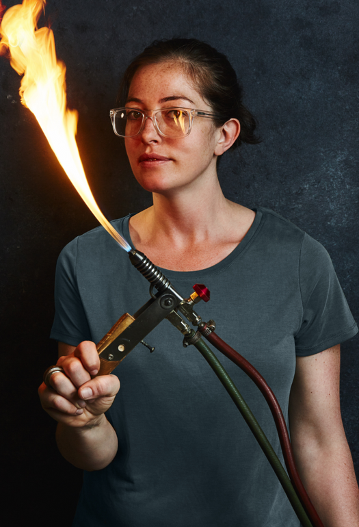 A woman in a grey shirt holding a torch with a flame