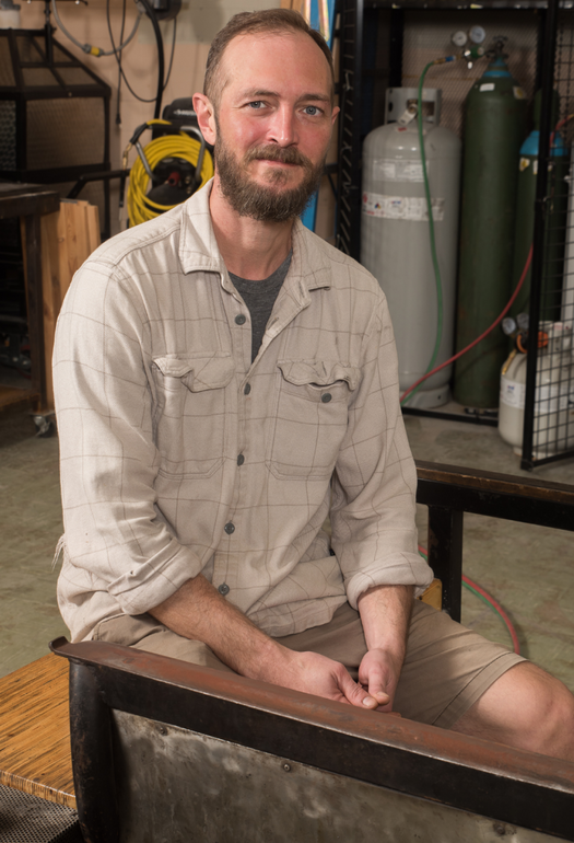 A man in a light brown button up shirt sitting on a brown bench