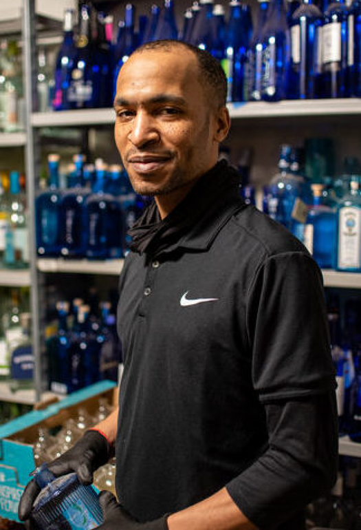 A man in a black sweater standing in front of a wall of blue bottles