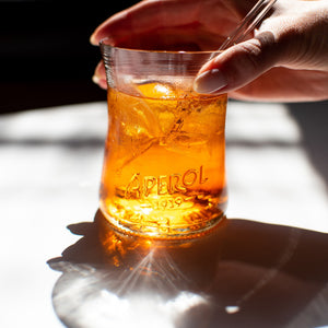 handmade recycled Aperol glass sitting on white table with aperol spritz and glass straw in it