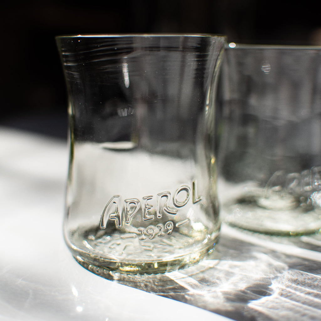 handmade recycled Aperol glass sitting on white table with aperol details embossed on the glass