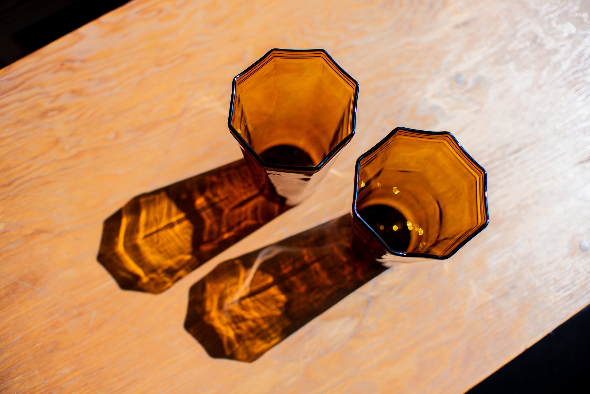 two amber recycled glass water cups with octagon top sitting on wood table with light reflections on table