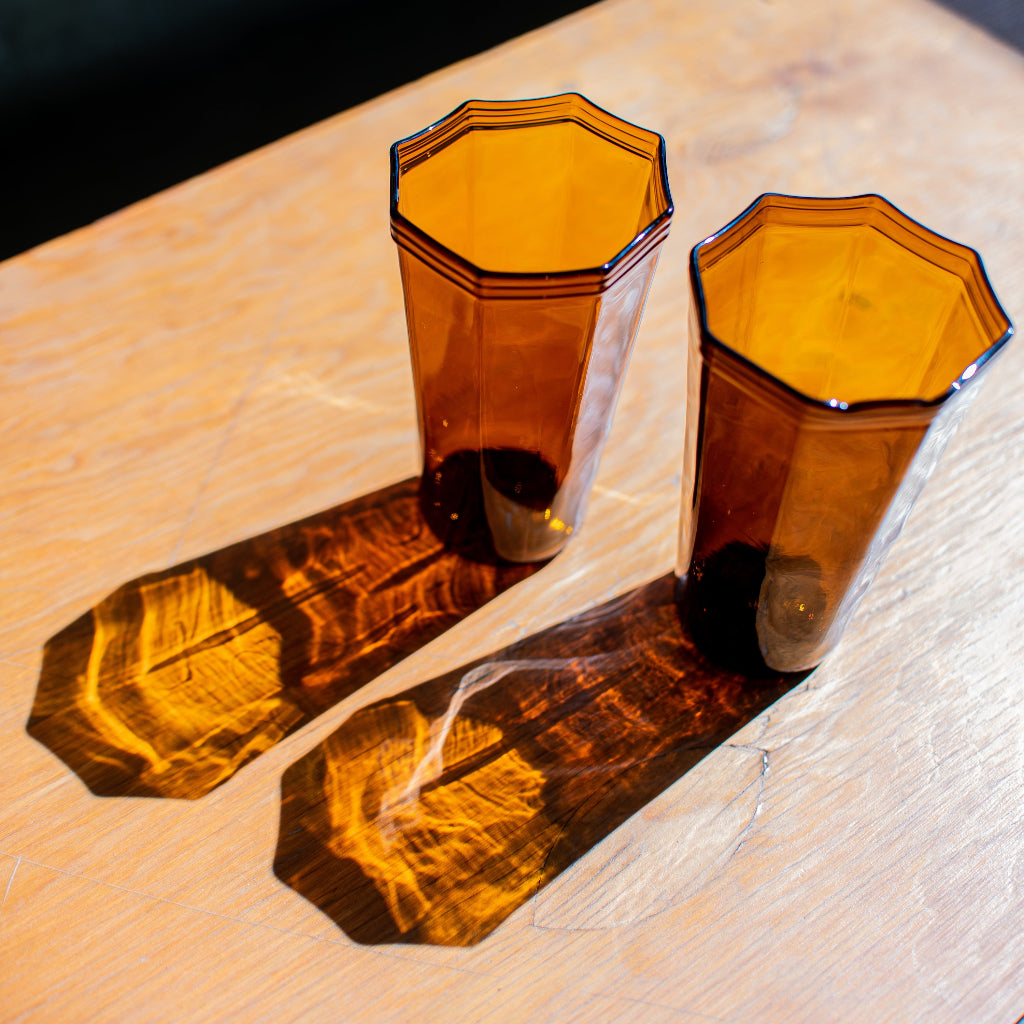 two amber recycled glass water cups with octagon top sitting on wood table with light reflections on table