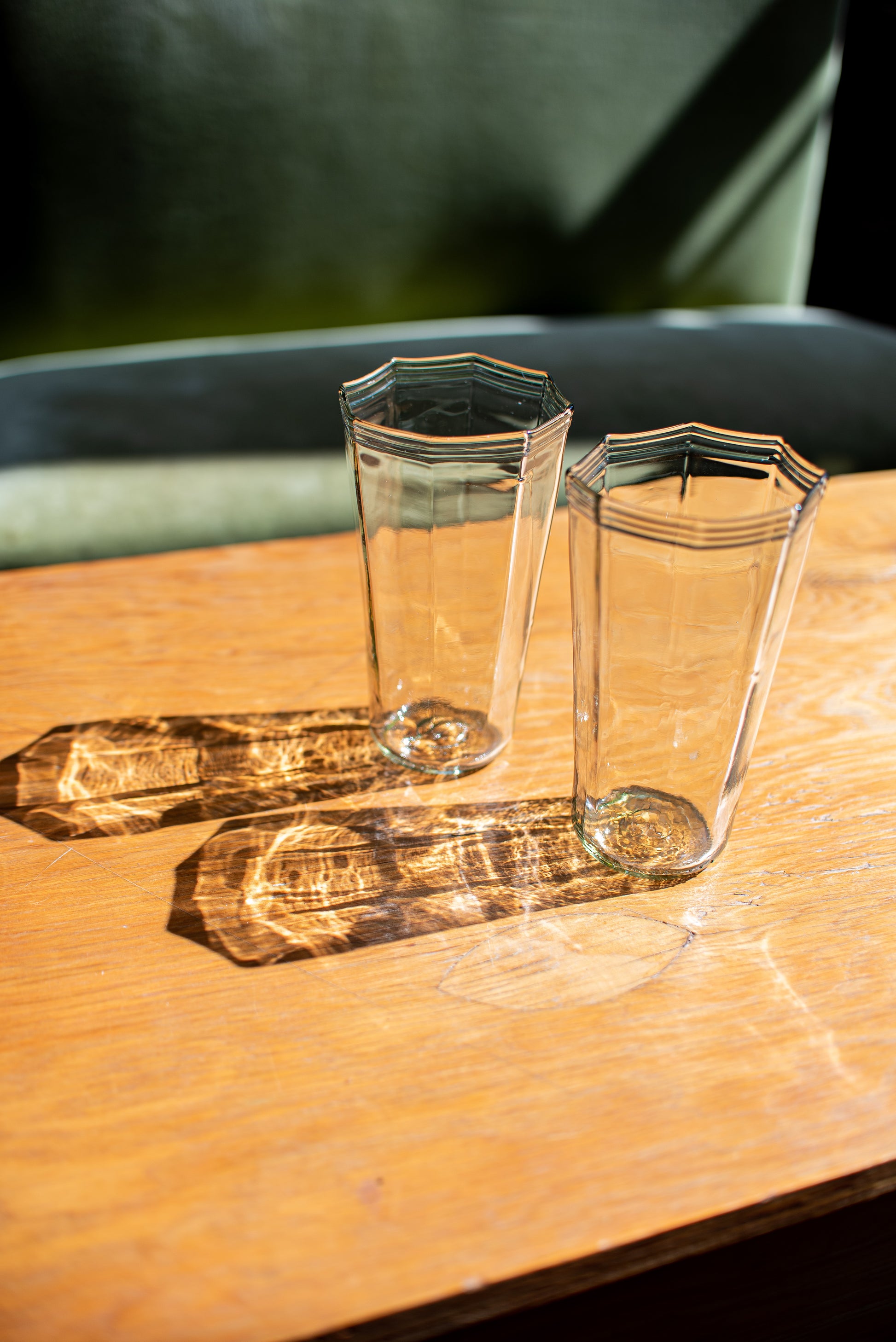 two recycled glass water cups with octagon top sitting on wood table with light reflections on table