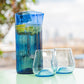 Blue glass vase and two clear glasses on a table with a blurred natural background