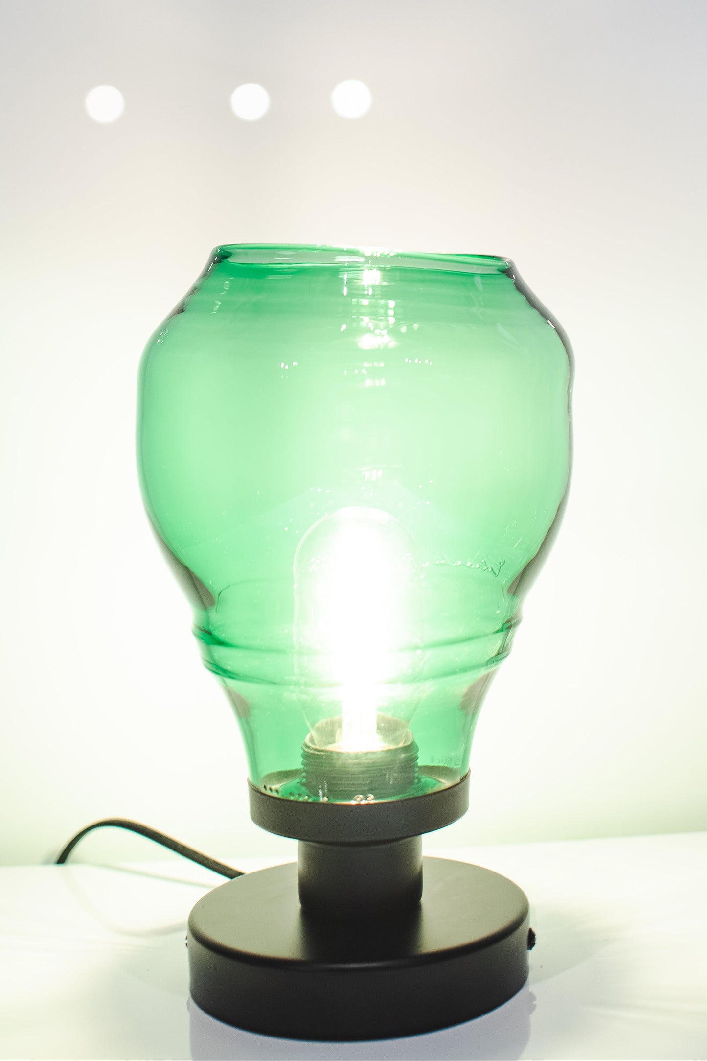 Green glass bottle repurposed as a lamp on a white background