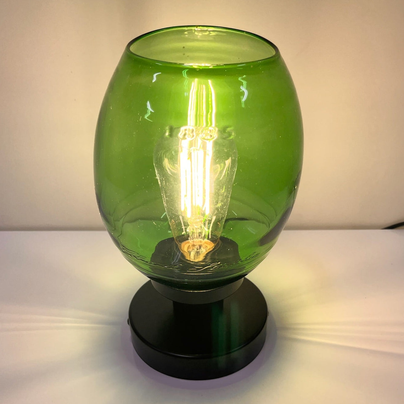 Green glass table lamp with a black base on a white surface.