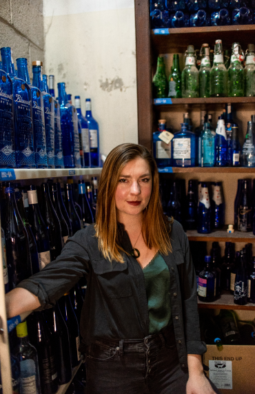 A woman in a black blazer standing in front of a wall of blue bottles