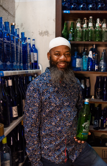 A man in a button up shirt standing in front of a wall full of blue bottles