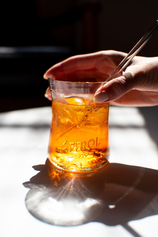 handmade recycled Aperol glass sitting on white table with aperol spritz and glass straw in it