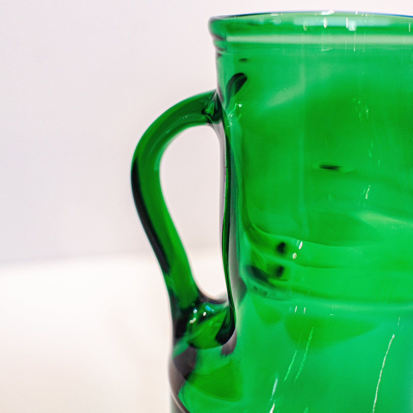 Green glass pitcher on a white background closeup of handle