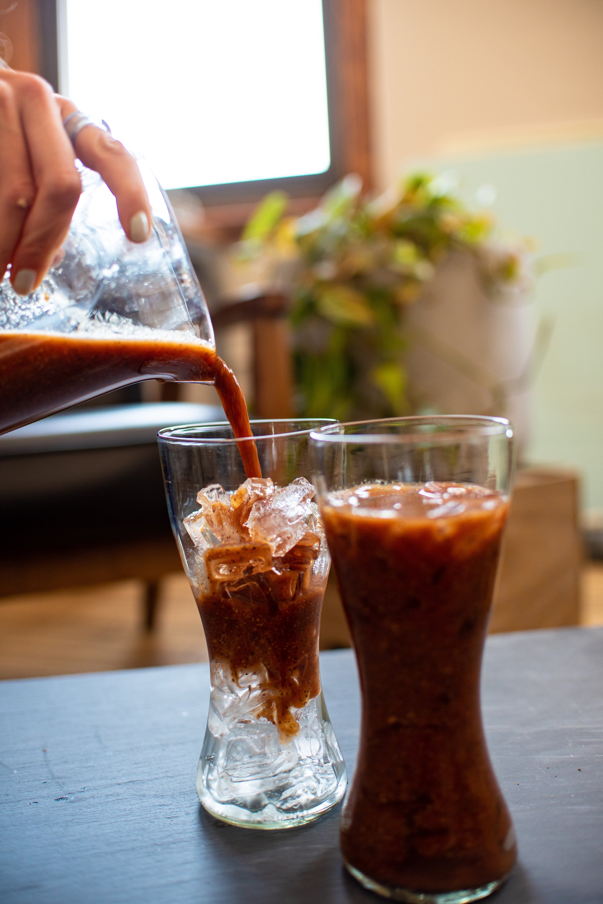 pitcher of bloody mary mix pouring into two recycled glasses made from Tito's bottles