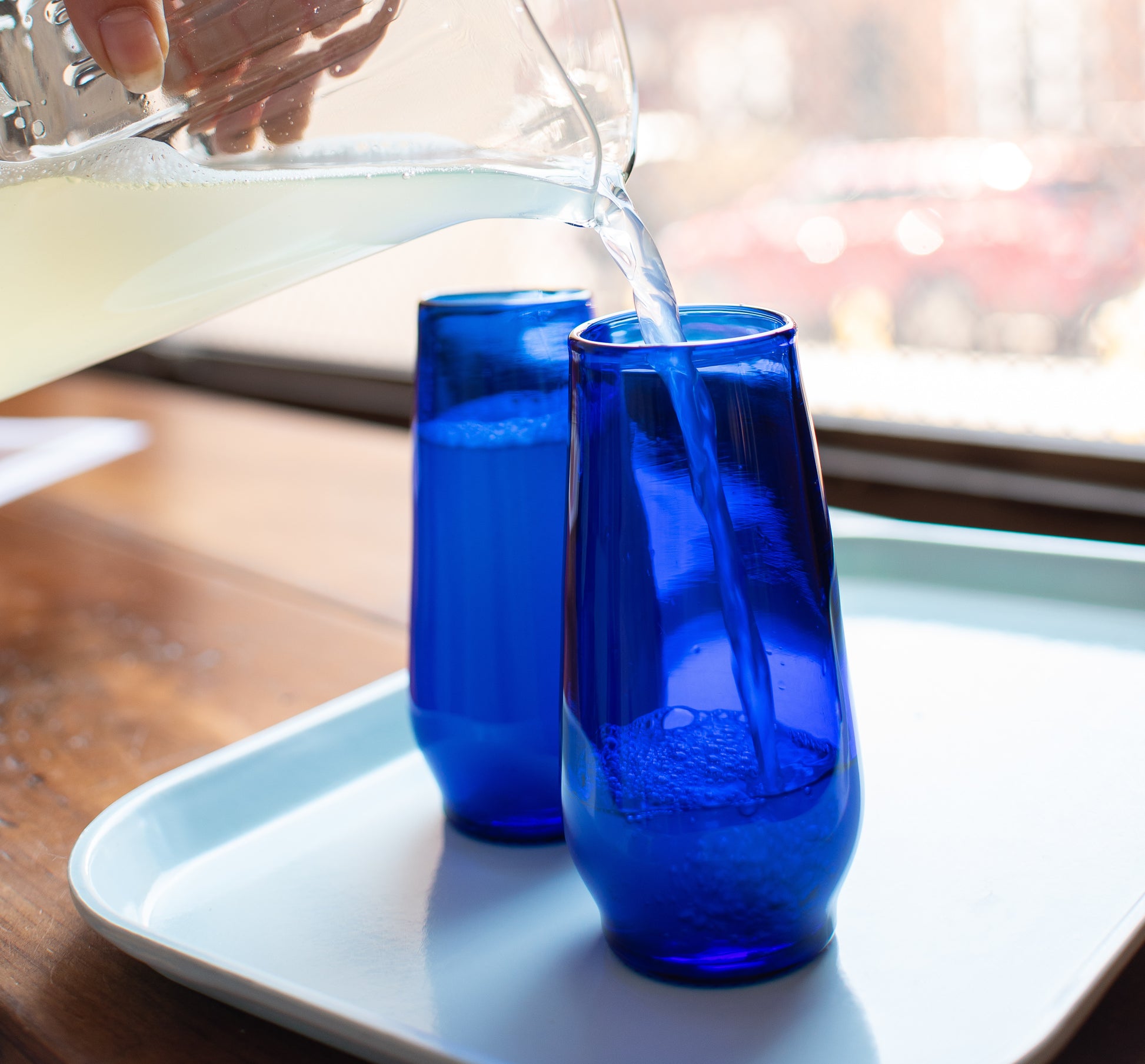 cobalt blue champagne flutes made from recycled glass with lemonade being poured from recycled glass pitcher