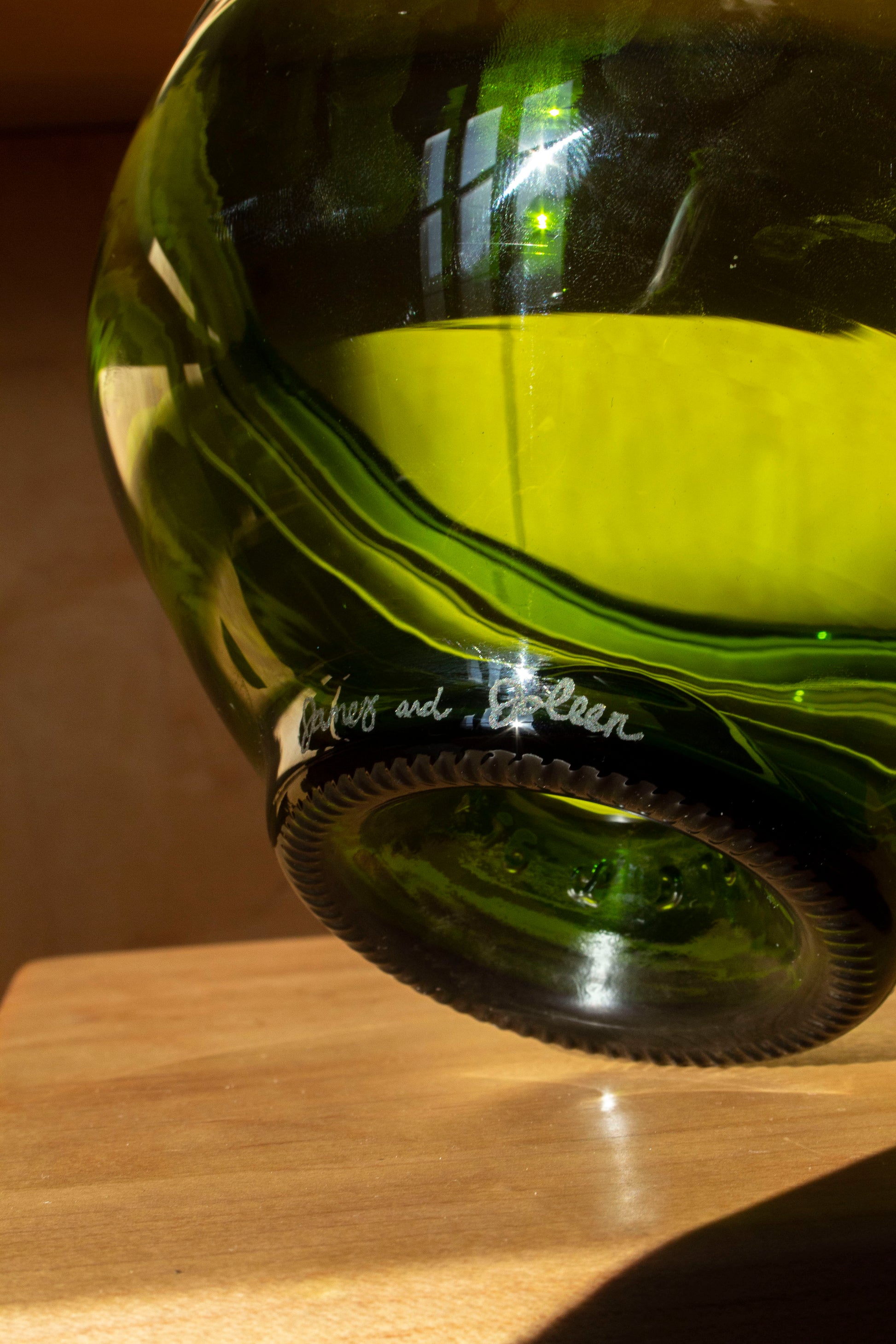 A close up photo of a serving bowl made from a recycled bottle highlighting the engraving that says two peoples names. 