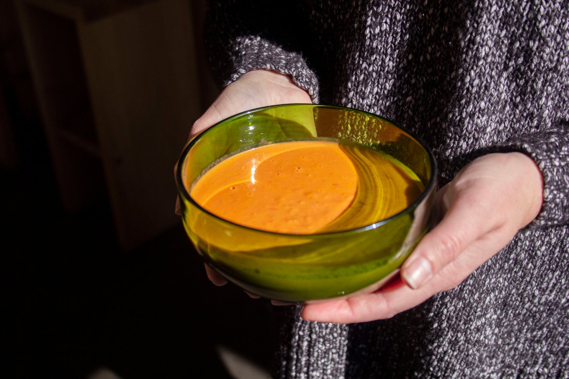 A small bowl made from recycled bottles in the color emerald with tomato soup in it. 