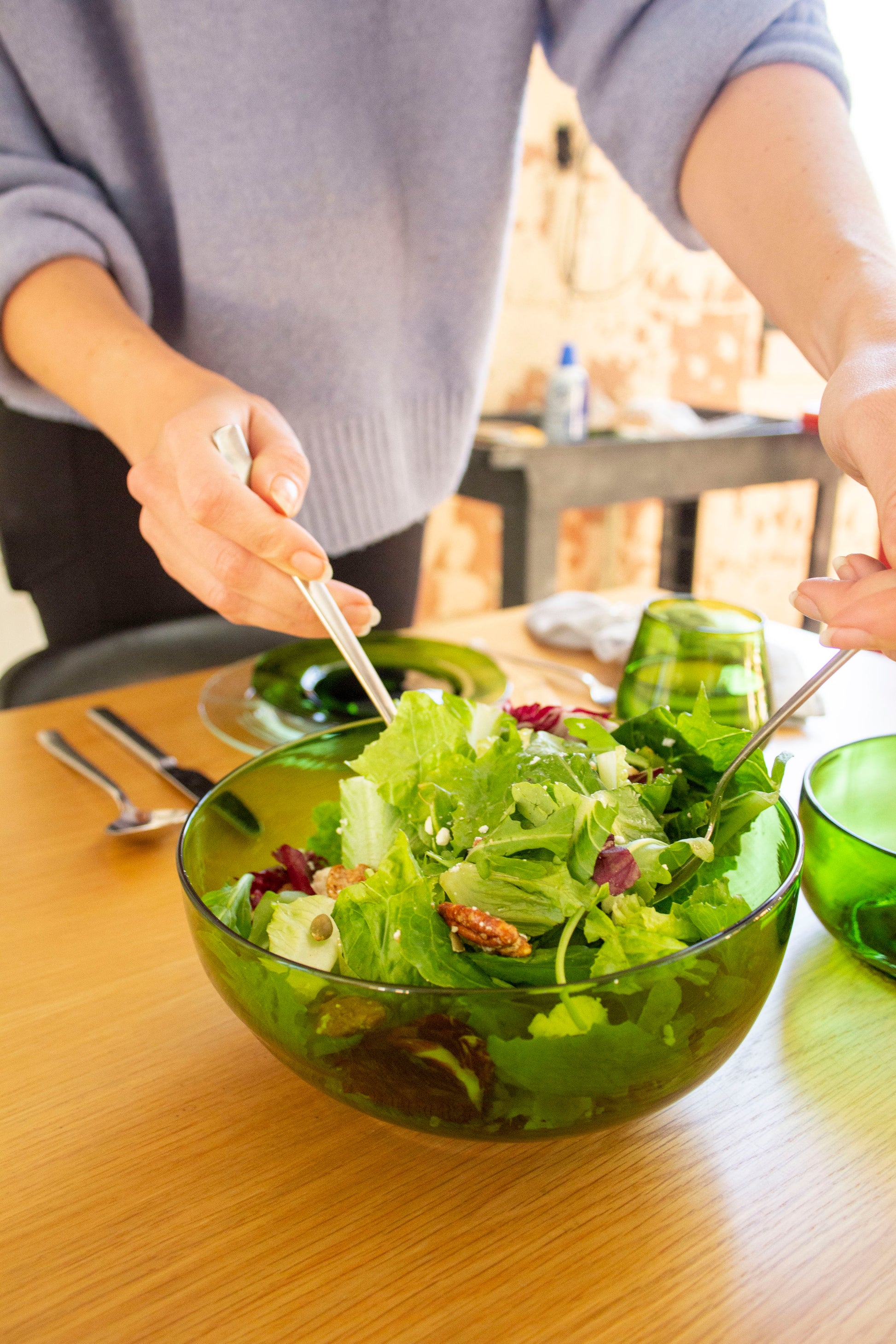 A person serving salad from a large nesting bowl made from an emerald recycled bottle