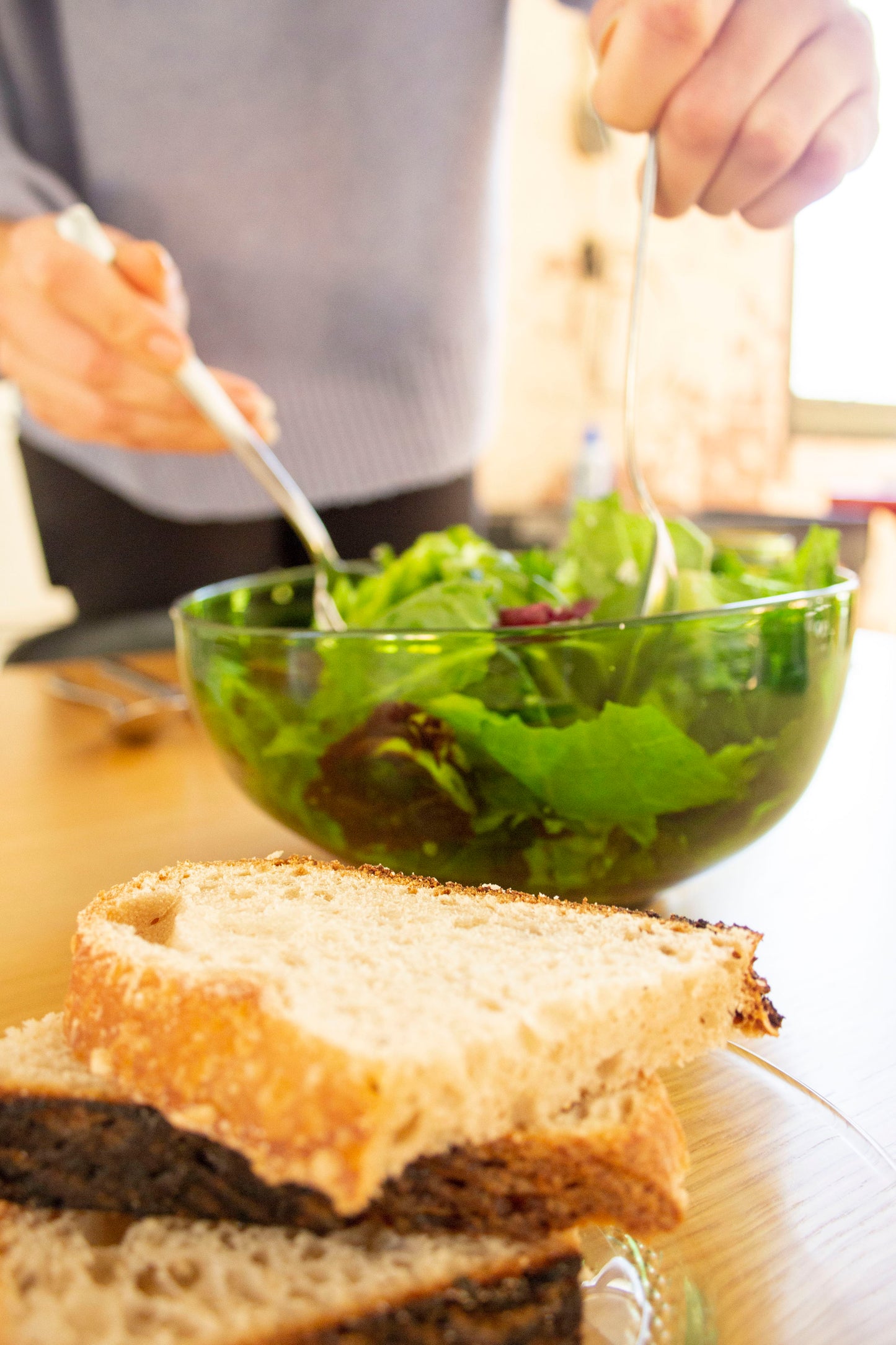 A person serving salad from a large nesting bowl made from an emerald recycled bottle